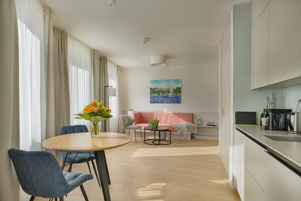 A modern living room with a round wooden table, two blue chairs, a pink sofa, and a painting on the wall.