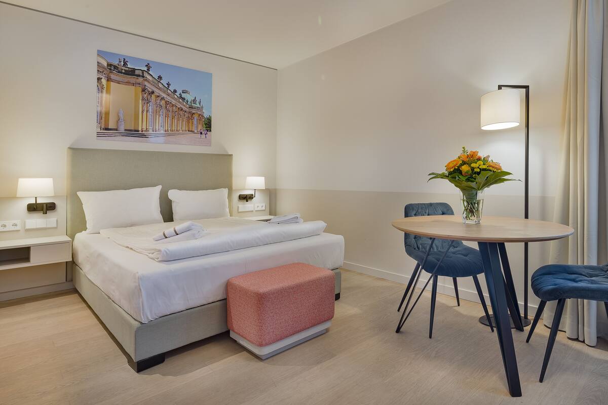 A hotel room with a bed, bedside tables, a small round table with chairs, and a vase with flowers.