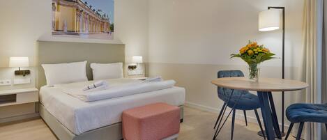 Habitación de hotel con cama, mesitas de noche, una pequeña mesa redonda con sillas y un jarrón con flores.