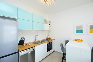 Uma cozinha moderna com armários brancos e azul-claros, bancada de madeira, pia, fogão e área de jantar com mesa e cadeiras brancas.
