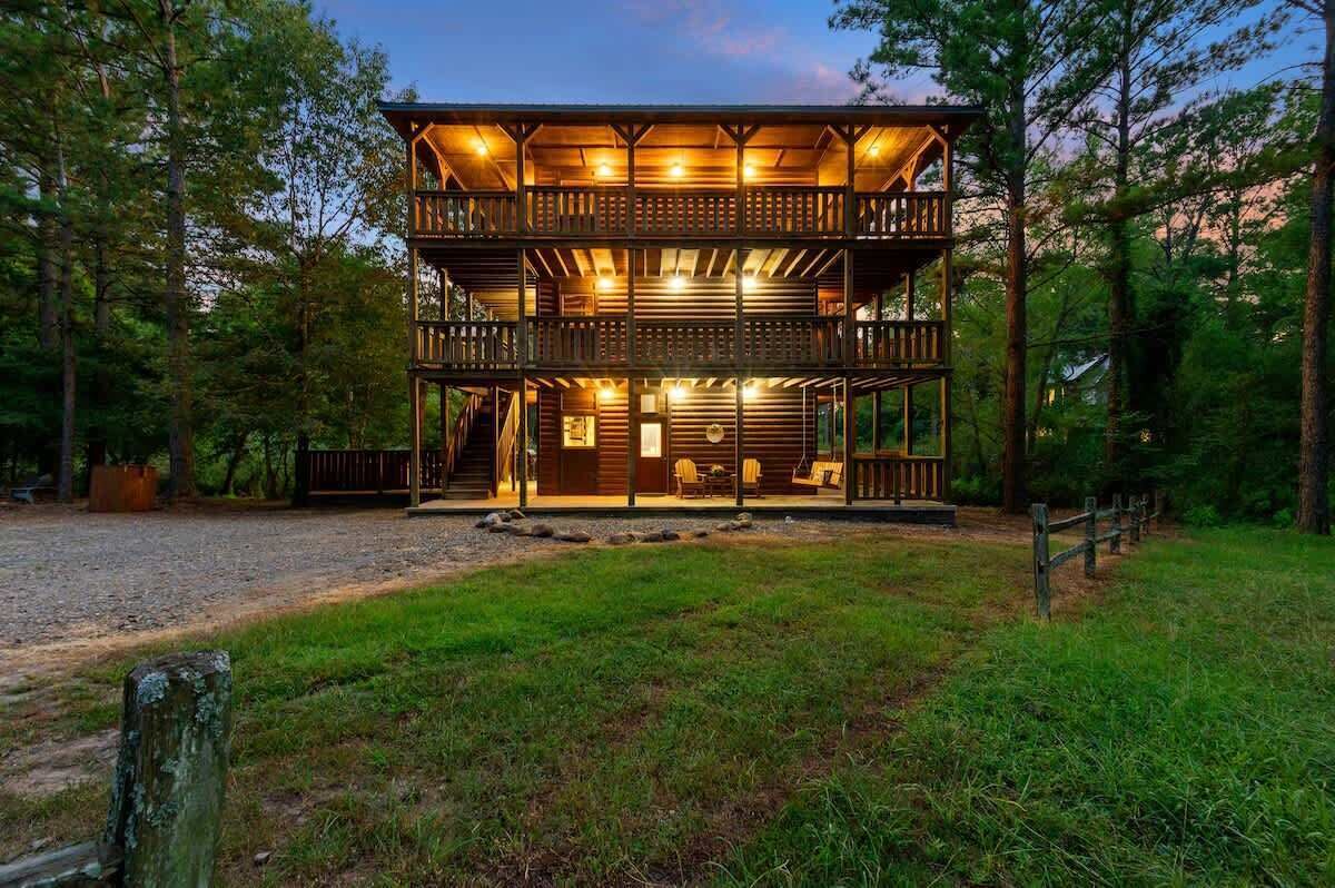 A two-story wooden cabin with a balcony, surrounded by trees.