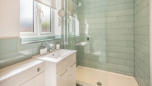 Une salle de bain moderne avec une douche à l’italienne en verre, un lavabo avec un miroir et une fenêtre.