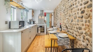 Une cuisine de taille réduite avec des meubles blancs, un plan de travail en bois et un mur en pierre.