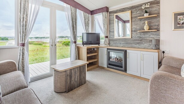 A modern living room with a fireplace, a television, and a large window with curtains. - 2 bedroom accommodation in Dornoch (Dornoch)