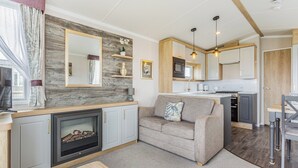 A modern living room with a fireplace, sofa, and a dining area with a table. - 2 bedroom accommodation in Dornoch (Dornoch)