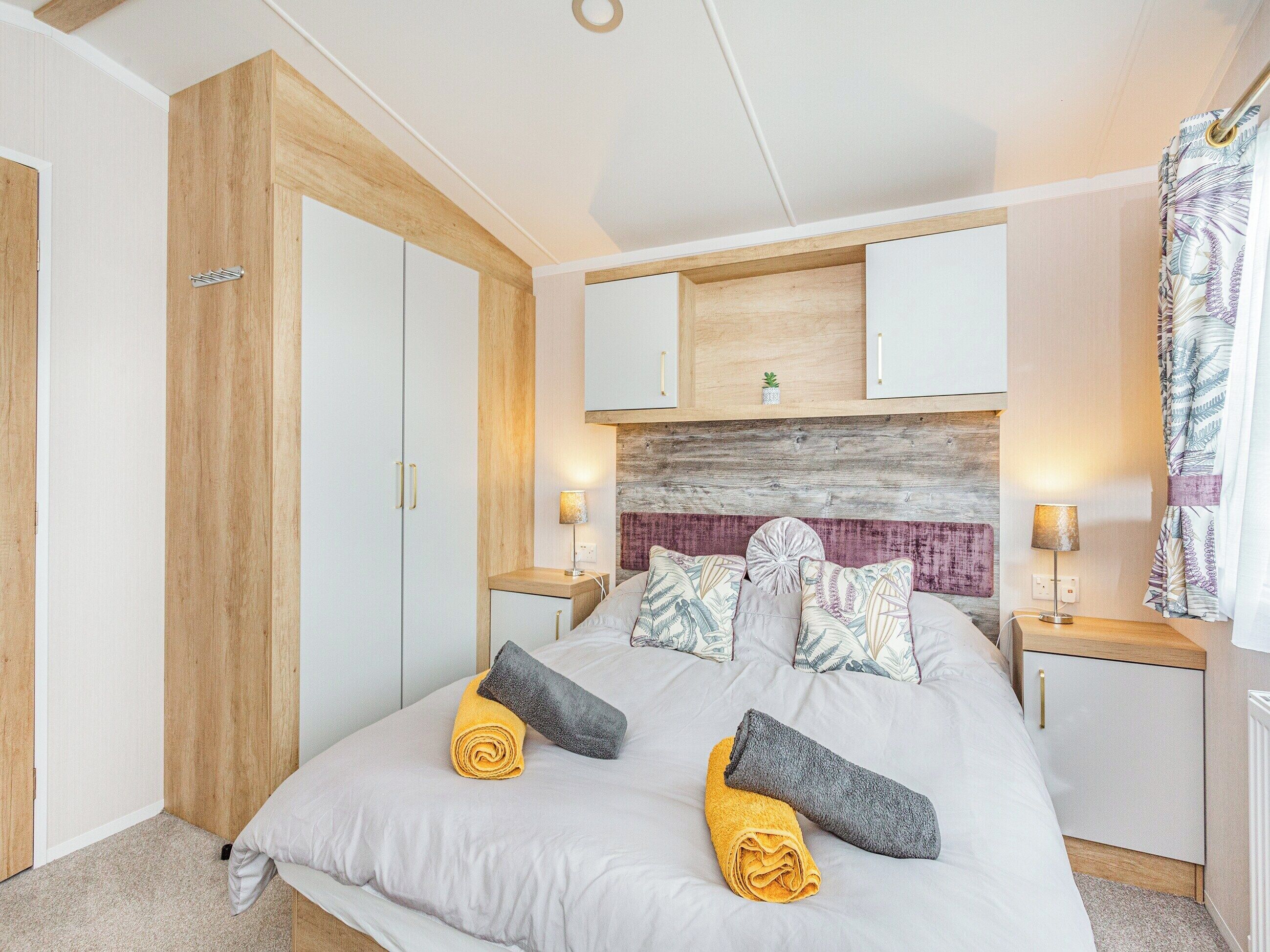 Un dormitorio con una cama, dos mesitas de noche, un armario de madera y un cabecero con panel texturizado.