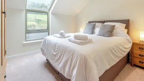 A bedroom with a large bed, a nightstand, a lamp, and a window with a view of greenery. - Property 3 - UK44923 (Ventnor)