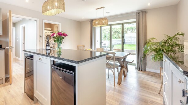 A modern kitchen with a central island, built-in dishwasher, and a dining area with a table and chairs. - Property 3 - UK44923 (Ventnor)