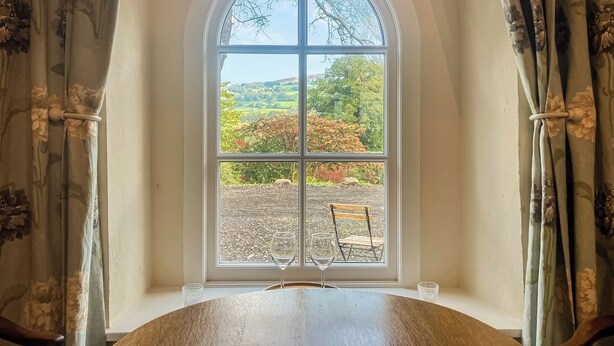 A room with a large arched window, a wooden table, and a chair. - The Chapel - UK45026 (Crickhowell)