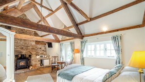 A bedroom with a stone fireplace, wooden beams, a bed, a desk, and a window with curtains. - The Chapel - UK45026 (Crickhowell)