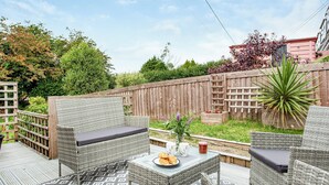 A patio with wicker furniture, a table with a plate of food, and a wooden fence in the background. - 2 bedroom accommodation in Foxhole, near St. Austell (Foxhole, near St. Austell)