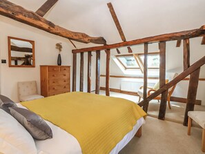 A bedroom with a bed, wooden beams, a dresser, a chair, and a skylight.