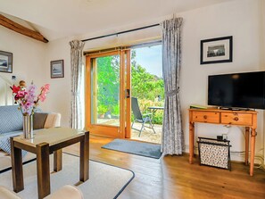 A living room with a sofa, a coffee table, a TV stand, and a sliding glass door leading to an outdoor area with plants.
