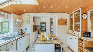 A modern kitchen with wooden ceiling, granite countertops, and a central island with fruits and a coffee machine.