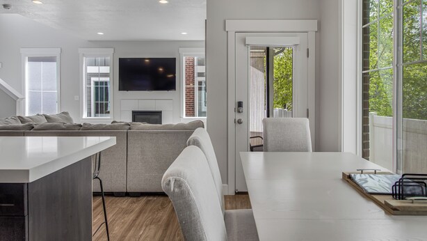 A modern living room with a white sofa, a dining table, and a flat-screen TV mounted on the wall. - New Modern Twin Home, Pet Friendly, Close to Airport, Downtown, Resorts and more (Millcreek)