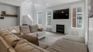 A modern living room with a sectional sofa, a fireplace, a flat-screen TV, and a staircase leading to an upper level. - New Modern Twin Home, Pet Friendly, Close to Airport, Downtown, Resorts and more (Millcreek)