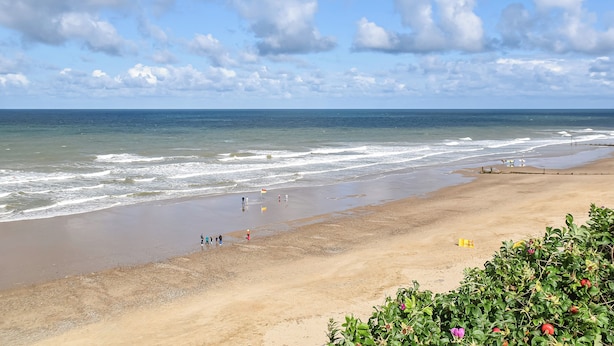 Une plage avec des vagues, un ciel dégagé et quelques personnes.