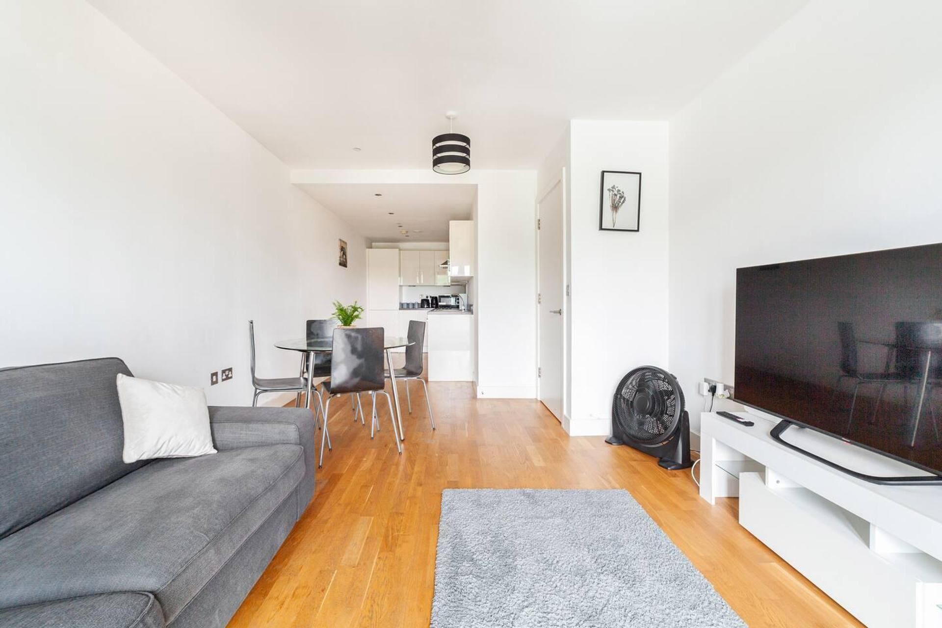 A modern living room with a grey sofa, a flat-screen TV, and a dining area with a small table and chairs.