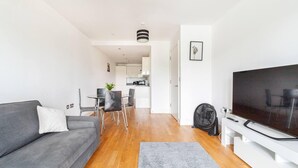 A modern living room with a grey sofa, a flat-screen TV, and a dining area with a small table and chairs.