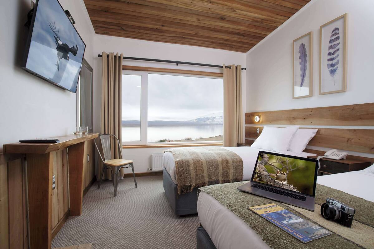 Habitación de hotel con cama, escritorio, silla, ordenador portátil, cámara y televisor.