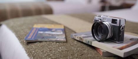 A camera on a bed with a magazine and a book.
