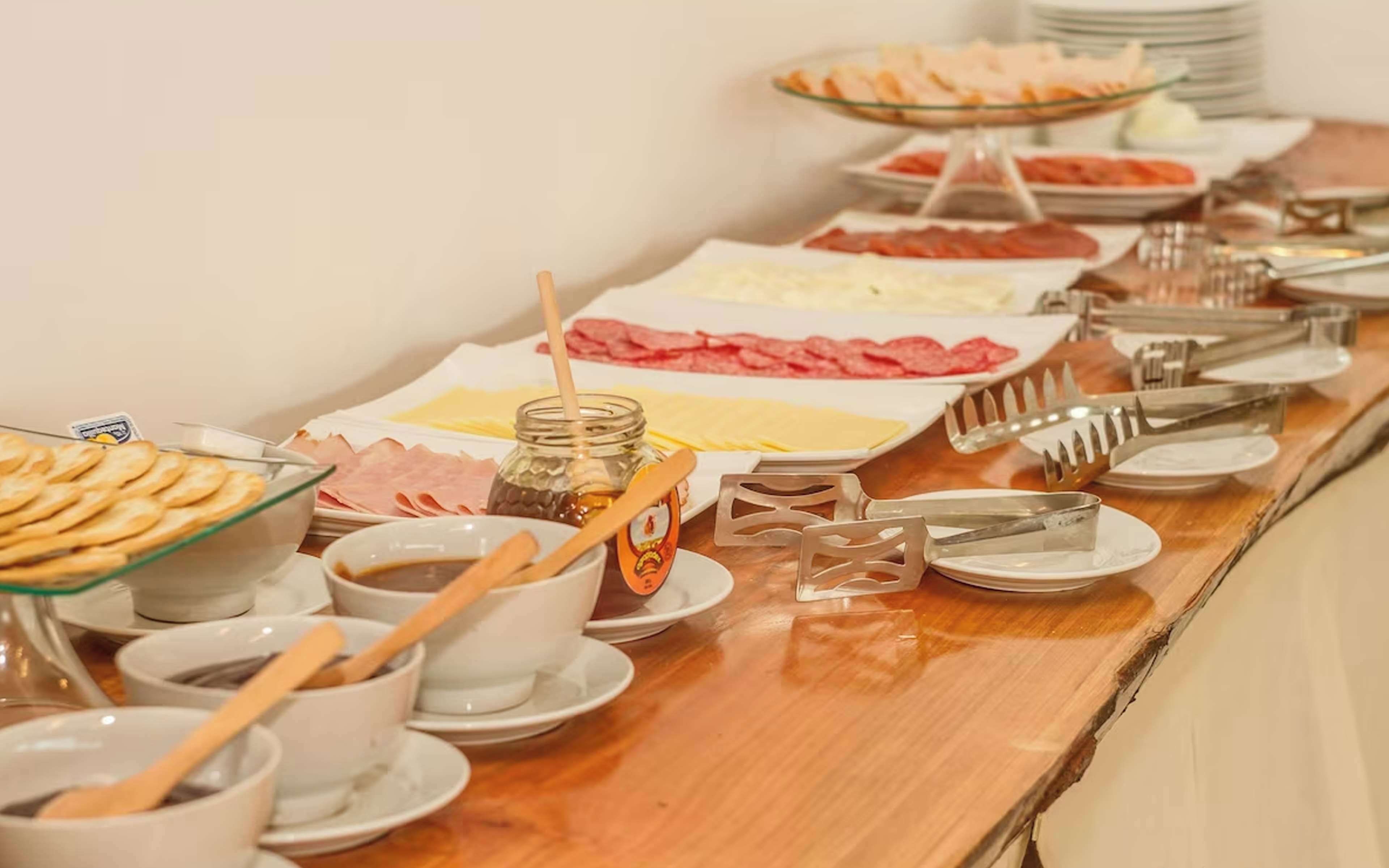 Una mesa de buffet con diversas opciones de comida, incluyendo carnes, quesos y salsas, además de utensilios para servir y vasos.