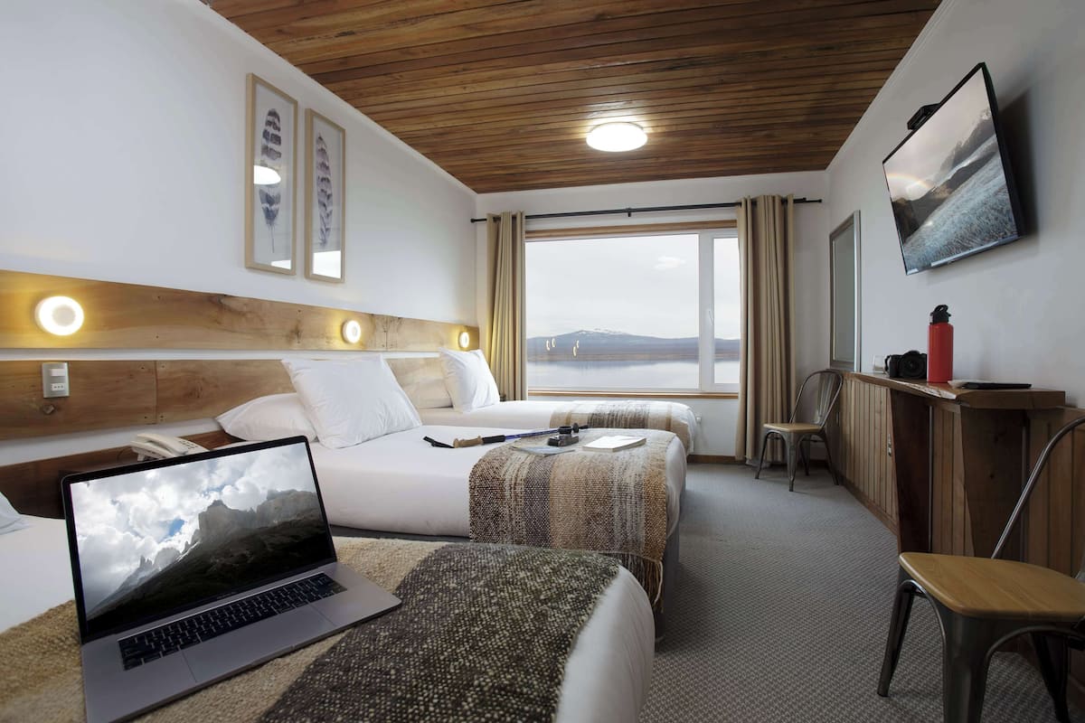 Habitación de hotel con dos camas, un escritorio, una computadora portátil y un ventanal con vistas a las montañas.
