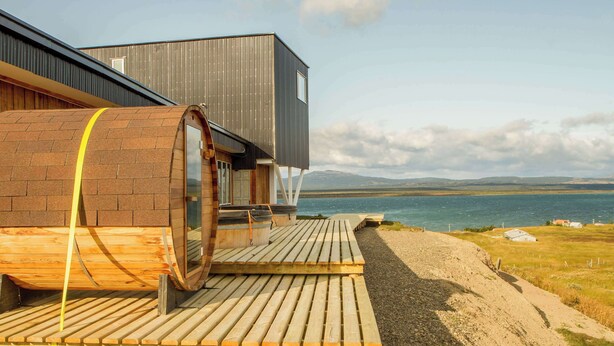 Un edificio moderno con terraza de madera y ventanas amplias con vistas a un cuerpo de agua.