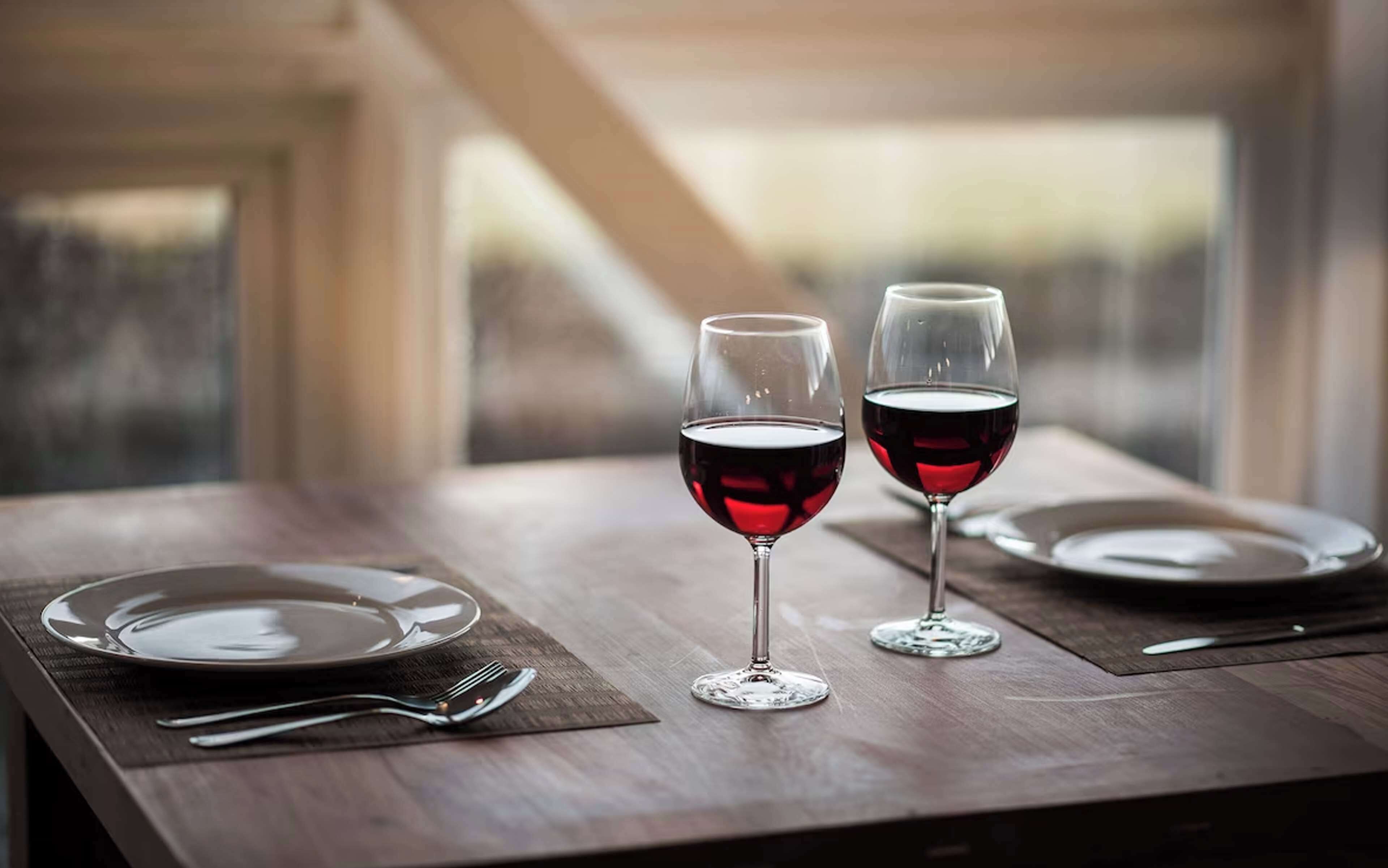A dining table with two wine glasses and a fork on a wooden surface.