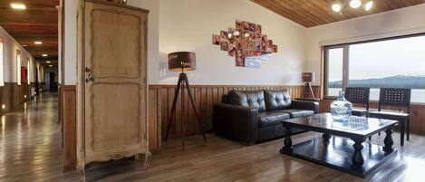 A spacious living room with a wooden floor, a large cabinet, a leather sofa, a coffee table, and a view of the outdoors.