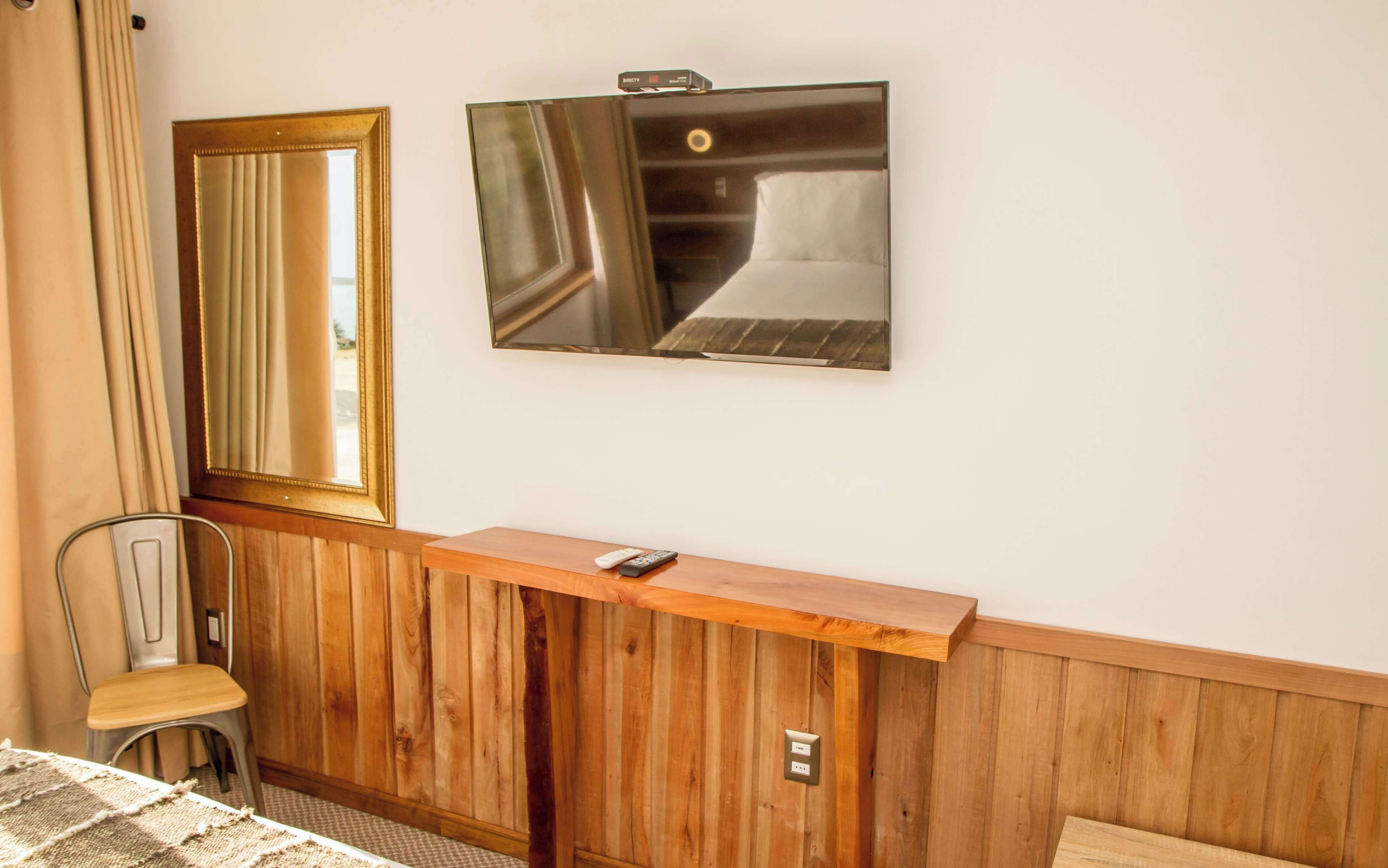 A hotel room with a wooden bench, a mirror, a television, and a chair.