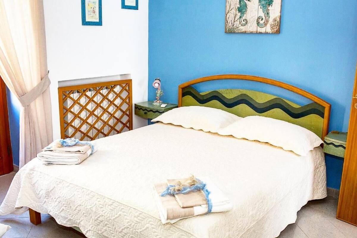 A neatly made bed with a white bedspread and pillows, a wooden headboard, and a nightstand with a lamp.