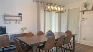 A modern dining area with a wooden table and chairs, a coffee machine, and a sign that says "WINE". - The Gathering Place PEC (Prince Edward)