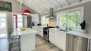 Une cuisine moderne avec des meubles blancs, un îlot central, des appareils en acier inoxydable et une grande fenêtre qui laisse entrer la lumière naturelle.