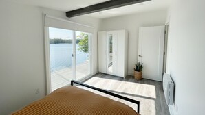 Une chambre moderne avec un lit, une porte-fenêtre coulissante donnant sur un balcon et une vue sur un lac.