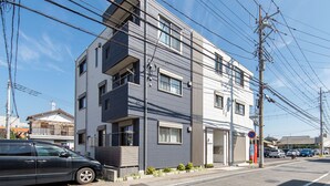 Un edificio moderno de dos pisos con fachada gris y blanca, entrada de garage visible y varios coches estacionados en la calle.