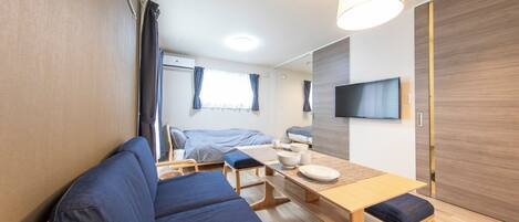 A modern, compact room with a sofa, a dining table, and a TV mounted on the wall.
