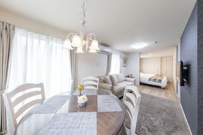 Una habitación moderna con mesa de comedor, sillas, candelabro, sofá, cama y aire acondicionado.