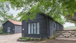 A small, dark wooden building with a single window, surrounded by gravel and a wooden gate. - 2 bedroom accommodation in Beauworth, near Alresford (Beauworth, near Alresford)