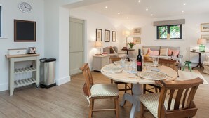 A dining area with a round table, chairs, and a bottle of wine. There is a sofa and a lamp in the background. - 2 bedroom accommodation in Beauworth, near Alresford (Beauworth, near Alresford)