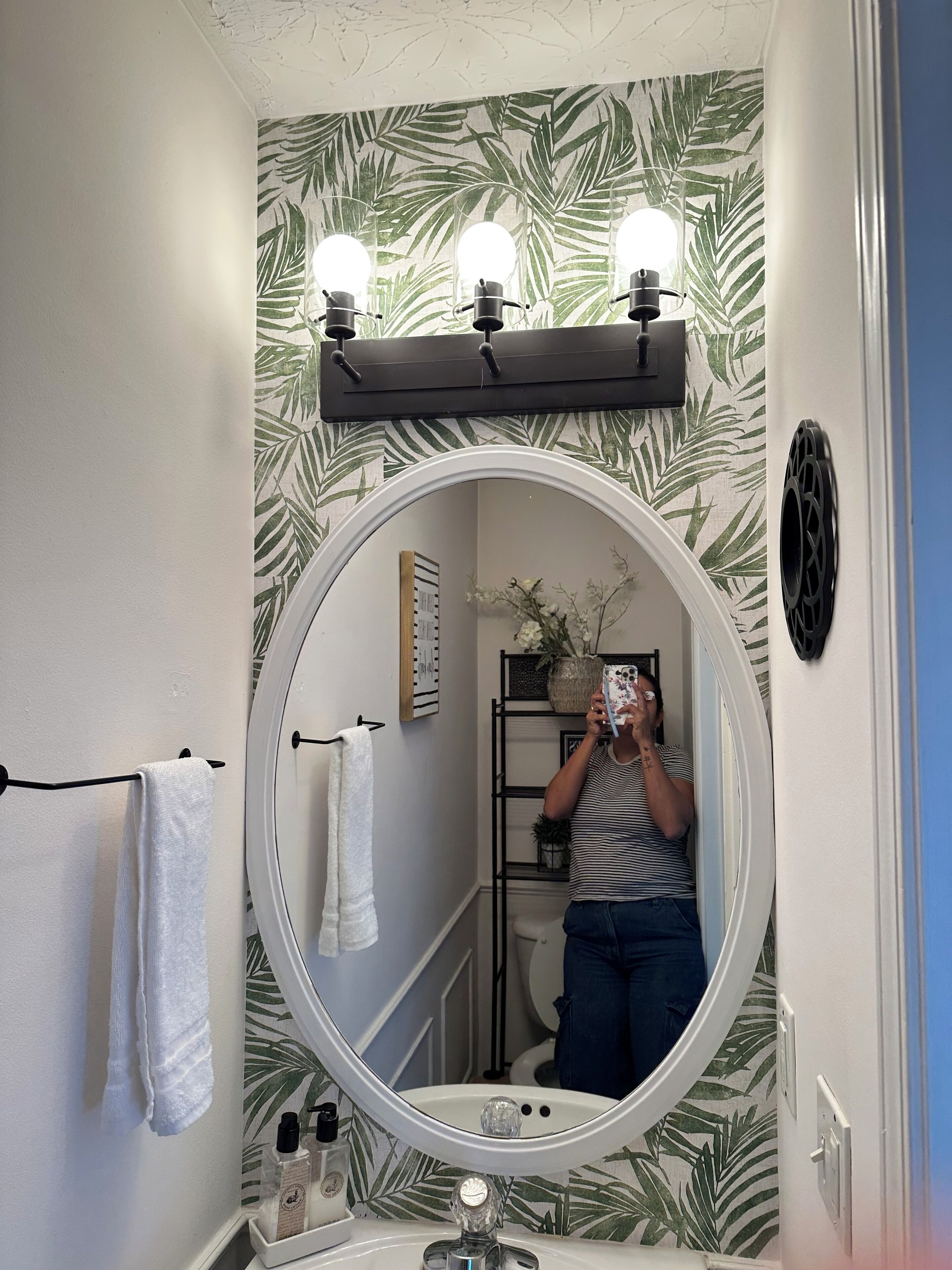Ein Badezimmer mit einem großen Spiegel, drei Wandleuchten, einem Handtuchhalter und einem Ablagefach mit Toilettenartikeln.