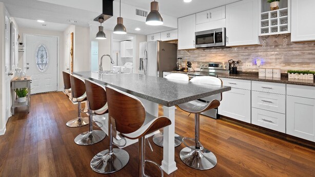 A modern kitchen with white cabinets, a central island with bar stools, stainless steel appliances, and pendant lighting.