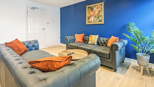 A living room with a dark blue sofa set, a coffee table, and a potted plant. - 2 bedroom accommodation in Blackpool (Blackpool)