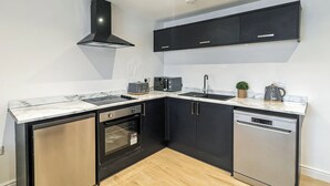 A modern kitchen with black cabinetry, a built-in oven, a dishwasher, and a marble countertop. - 2 bedroom accommodation in Blackpool (Blackpool)