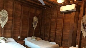 Une chambre de style cabane en bois, équipée de trois lits, d’un ventilateur de plafond et d’un climatiseur fixé au mur.