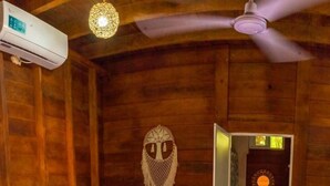 Une chambre de style cabane en bois, équipée d’un lit, d’un ventilateur de plafond, d’un appareil de climatisation et d’une salle de bain avec un lavabo et un miroir.