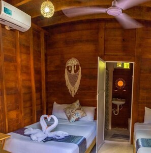 A wooden cabin room with a bed, a ceiling fan, an air conditioning unit, and a bathroom with a sink and mirror. - Cabanas Chac Mool (Isla Holbox)