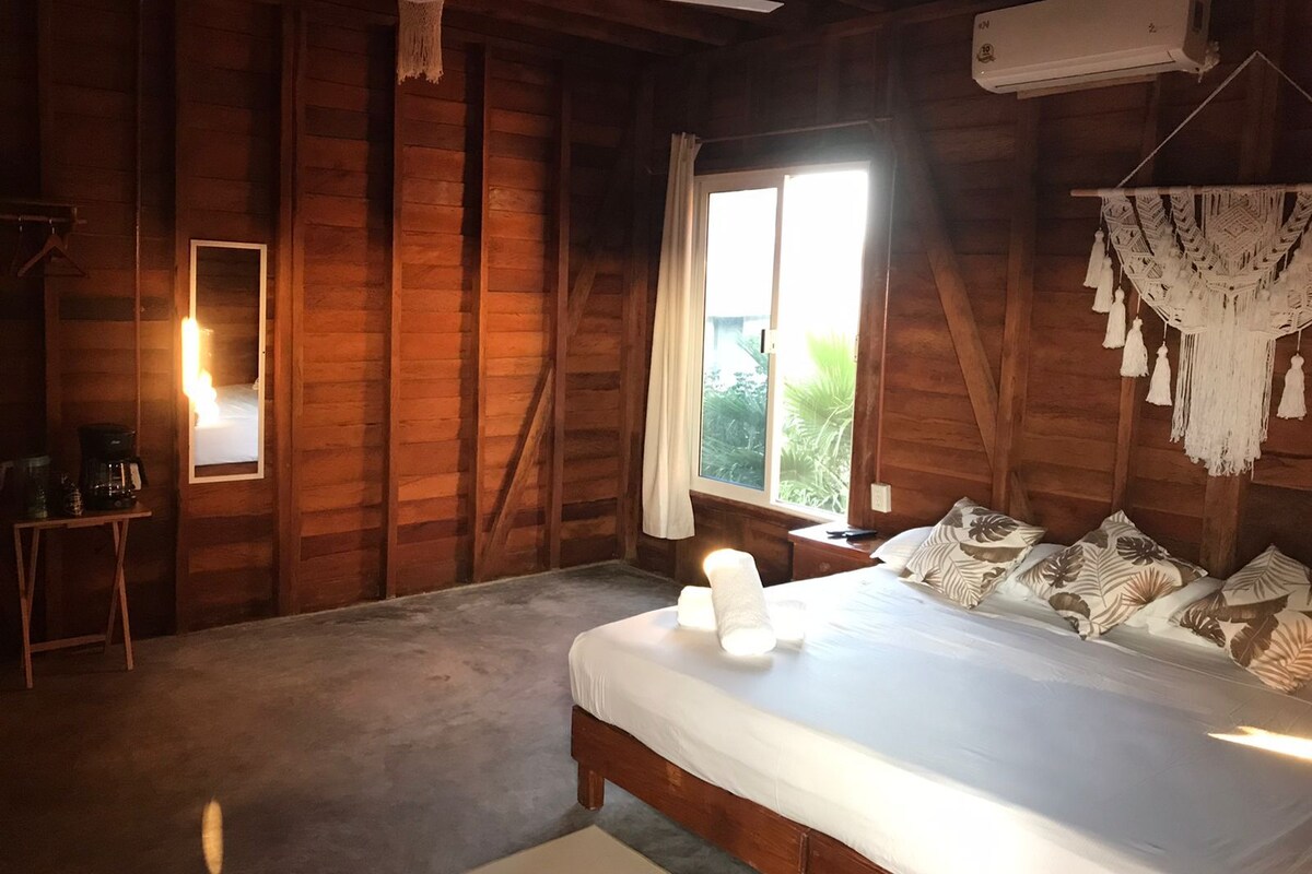 A wooden cabin bedroom with a bed, a ceiling fan, a window, and a wall-mounted air conditioner.