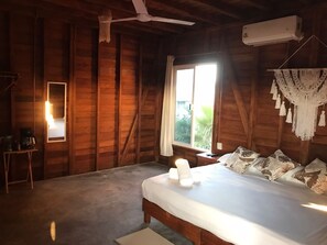 A wooden cabin bedroom with a bed, a ceiling fan, a window, and a wall-mounted air conditioner.