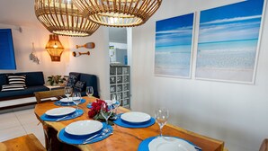 Un coin repas avec une table en bois dressée pour quatre personnes, des sets de table bleus, des assiettes blanches et des verres à vin.